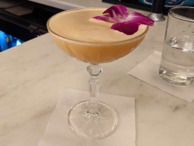 The "Catch Me Out Chai" cocktail, served in a coupe glass, with an edible flower floated at the top.